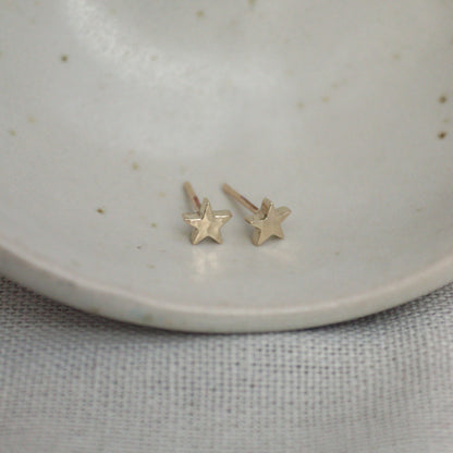 Little 9ct yellow gold star studs on a white bowl. The studs have a hammered finish.