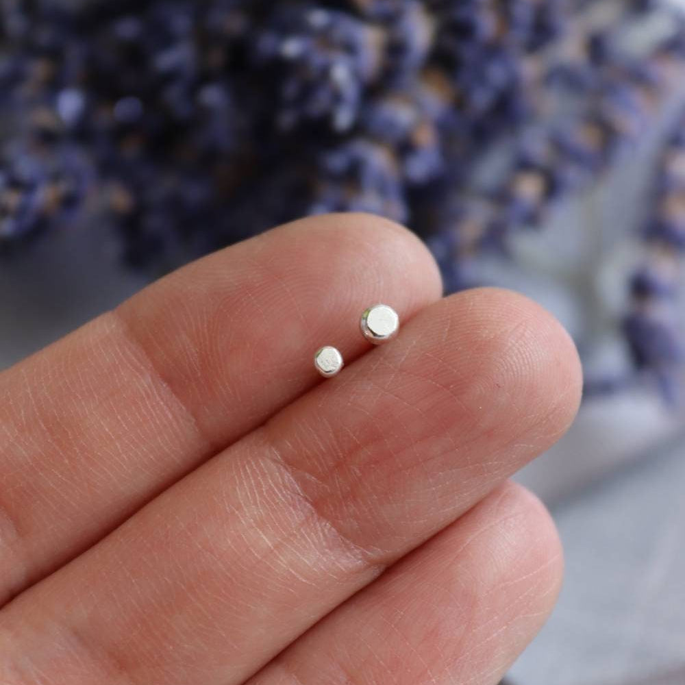 a 2.5mm and 3mm silver recycled dot stud held in a hand to show the size difference.