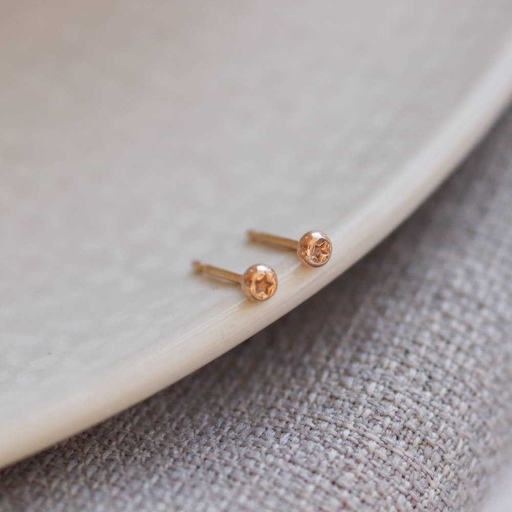 tiny dots of yellow gold star impression stud earrings on the side of a plate.