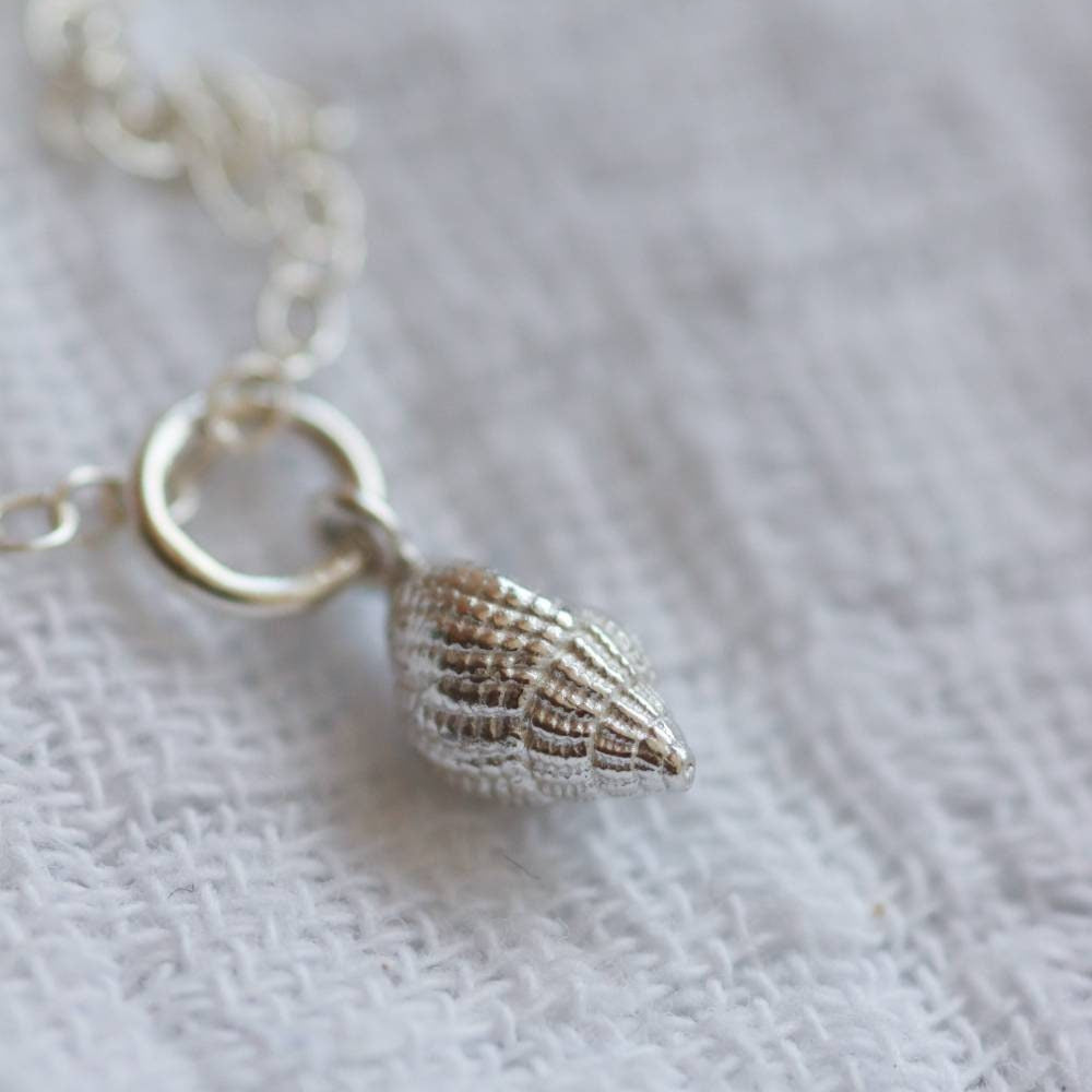 Close up of the detail of a silver dorset whelk pendant strung on a silver chain.