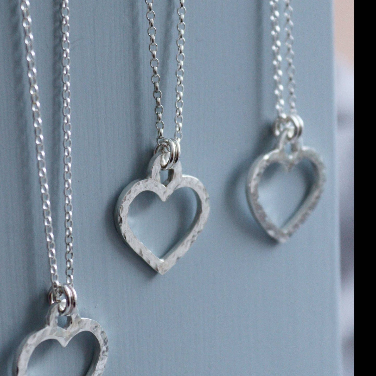 Hammered silver open heart necklaces on a grey background.