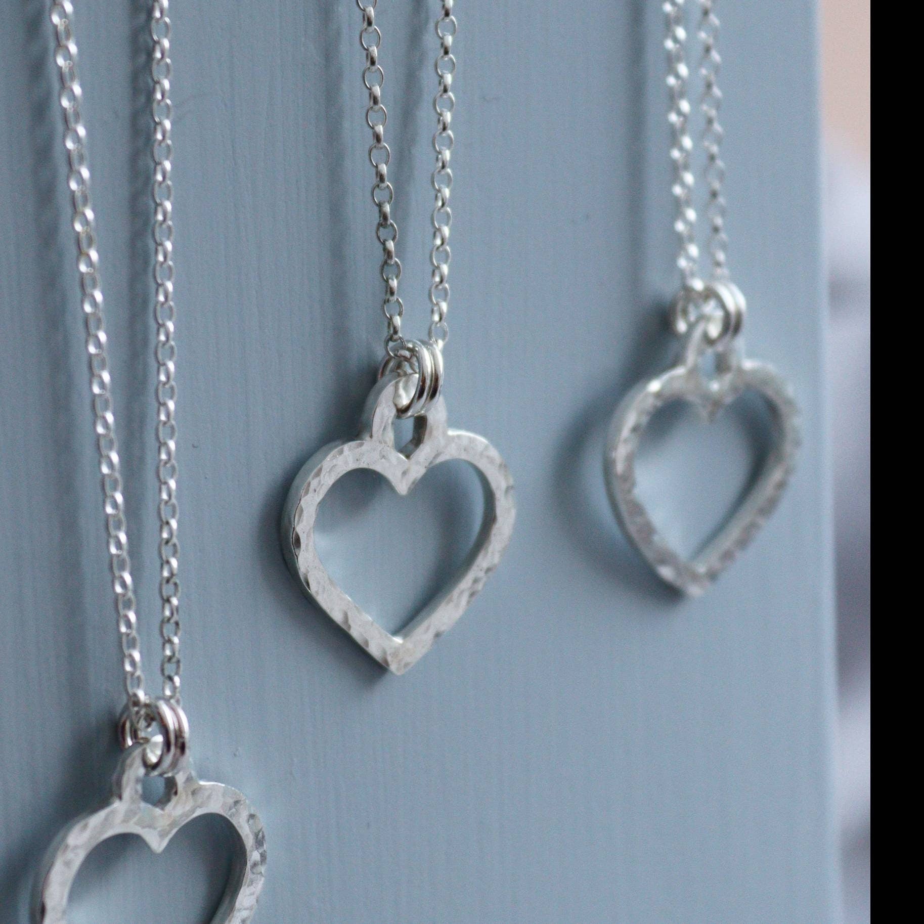 Hammered silver open heart necklaces on a grey background.