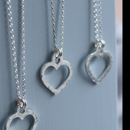 Hammered silver open heart necklaces on a grey background.