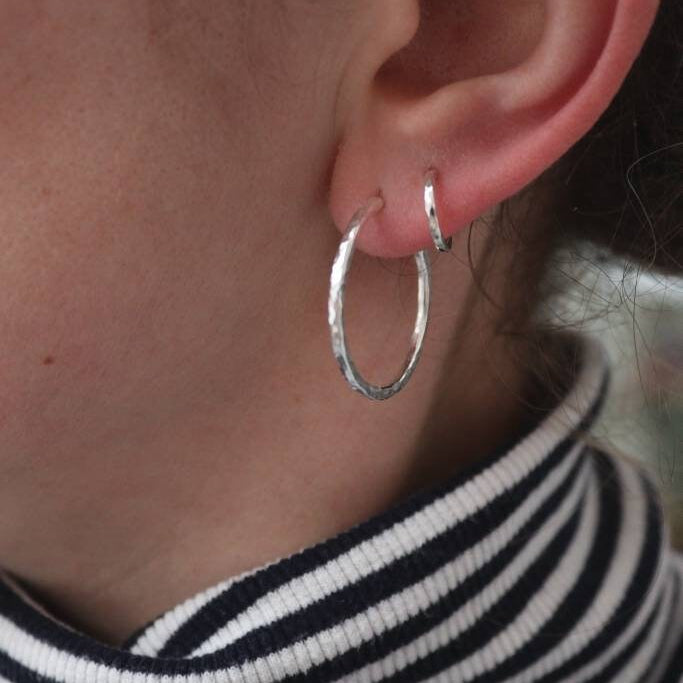 Shiny hammered silver hoops shown in a models ear, a large pair and a smaller pair.