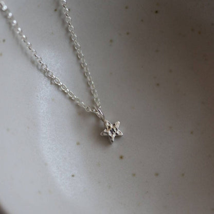 Hammered silver star pendant with an initial stamped on a fine silver chain on a light beige background.