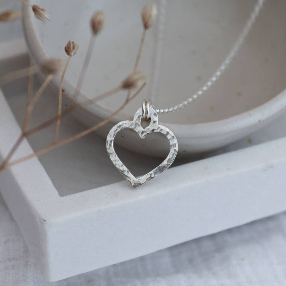 A silver hammered heart necklace with a chain, displayed against a neutral background.