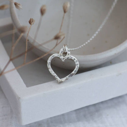 A silver hammered heart necklace with a chain, displayed against a neutral background.