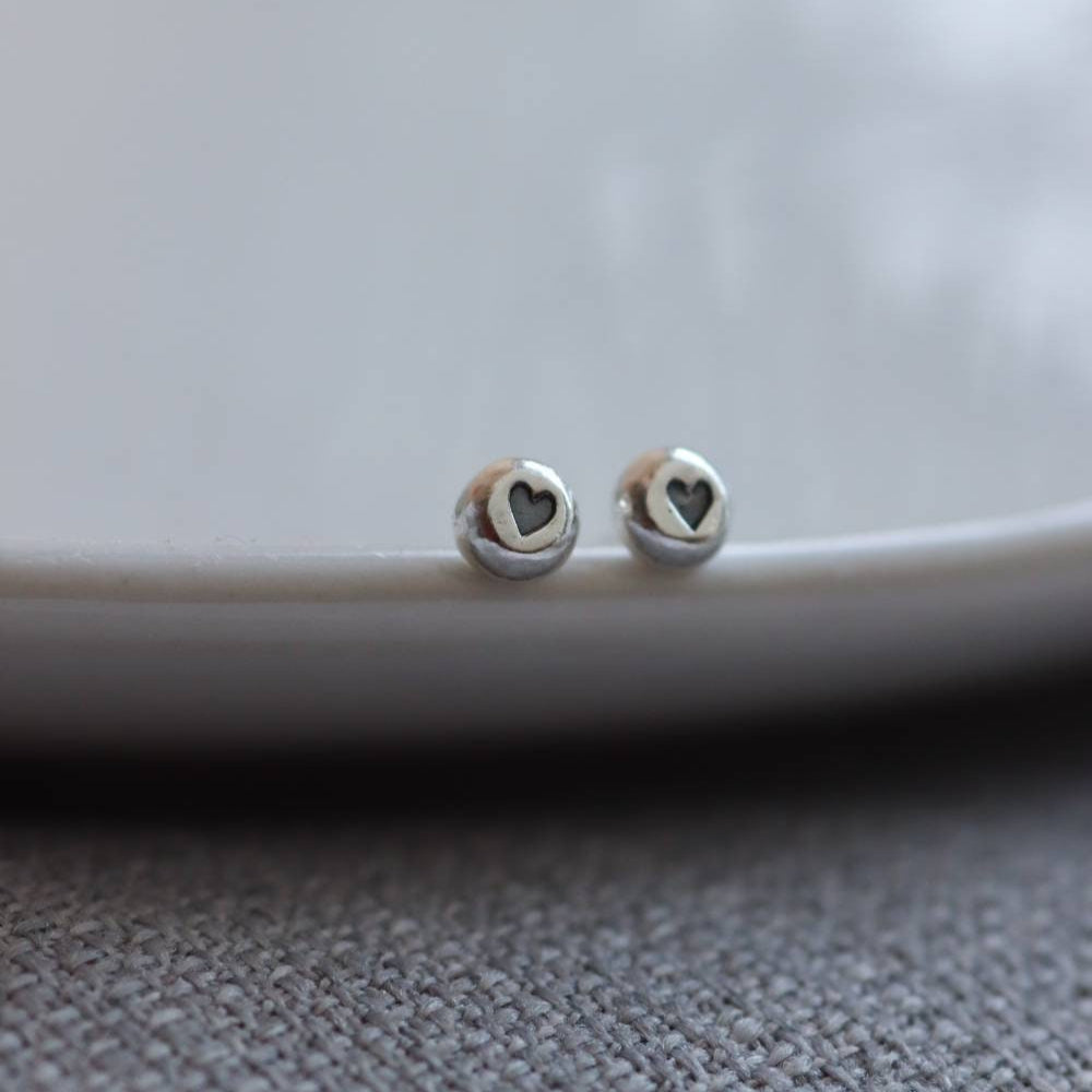 a pair of tiny silver studs with a heart shaped impression that is blackened for contrast.
