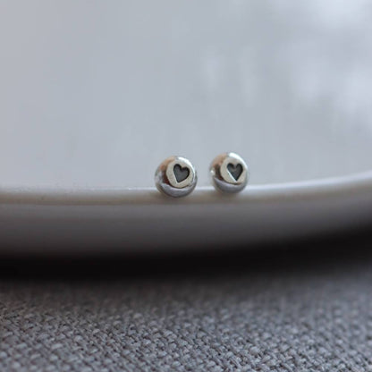 a pair of tiny silver studs with a heart shaped impression that is blackened for contrast.