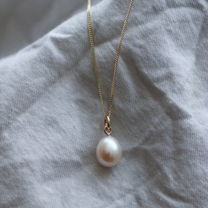 Large ivory pearl on a gold curb chain against crumpled fabric