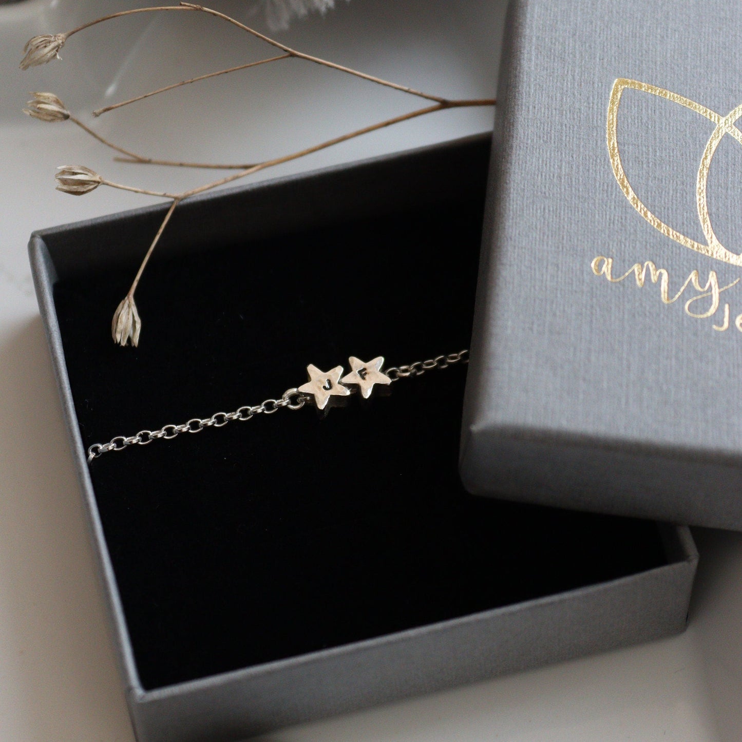 A silver chain with two star beads personalised with initials in a branded jewellery box.
