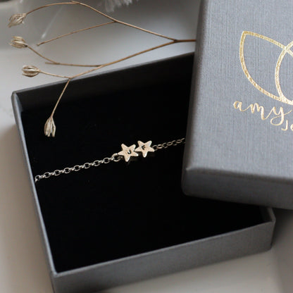 A silver chain with two star beads personalised with initials in a branded jewellery box.