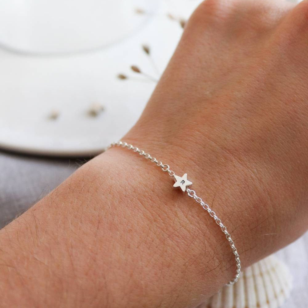 A silver chain bracelet with star charm in the middle with a letter stamped on the charm. Shown on a models wrist.
