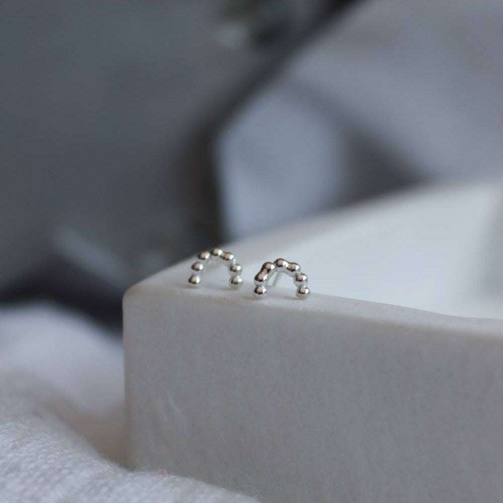 Minimalist Silver rainbow studs made from beaded wire on a marble tray.