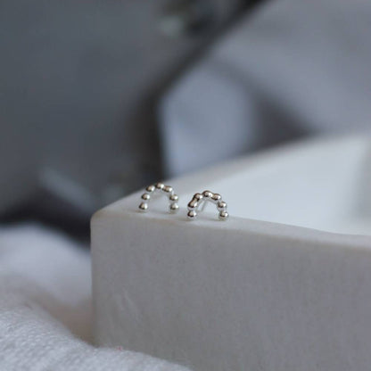 Minimalist Silver rainbow studs made from beaded wire on a marble tray.