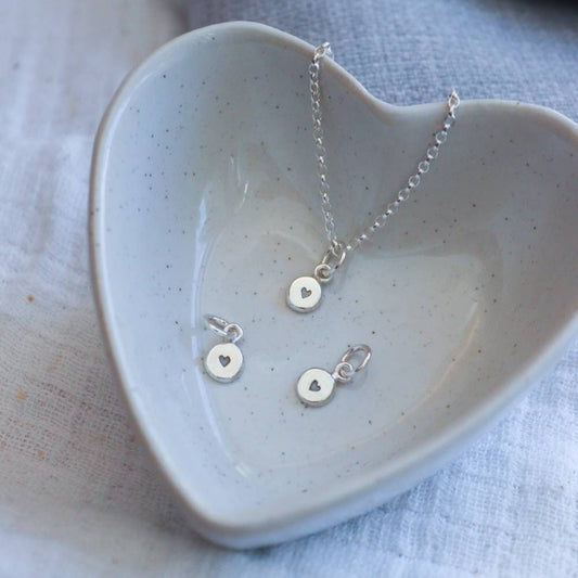 A round silver pendant with a heart impression stamped in the centre that is blackened. Shown as 