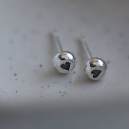 silver stud earrings with a heart stamp in the middle in contrasting black. 