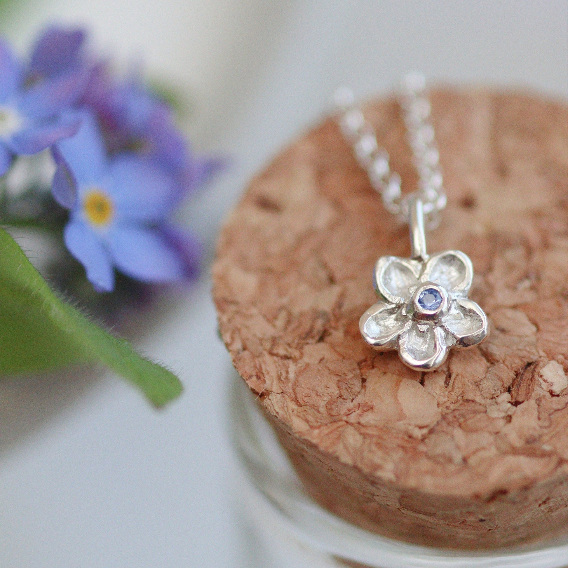silver handcarved forget-me-not pendant necklace with a cornflower blue sapphire centre.