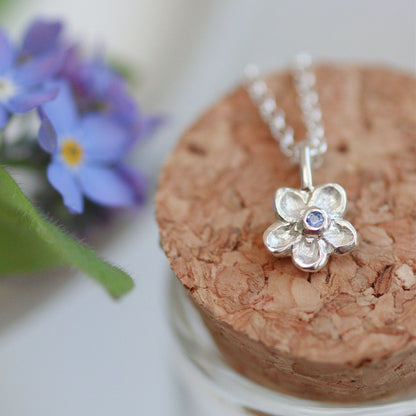 silver handcarved forget-me-not pendant necklace with a cornflower blue sapphire centre.
