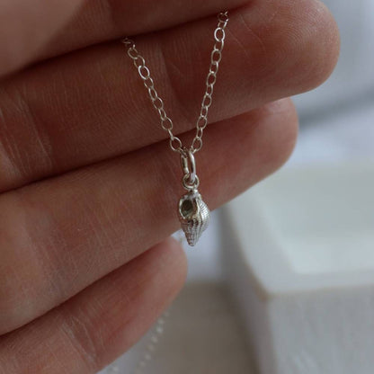 A tiny silver seashell on a fine trace chain being held up for the camera.