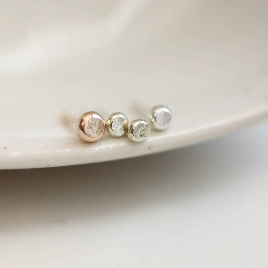 a row of 4 tiny dot stud earrings, yellow gold, white gold and silver with slight texture