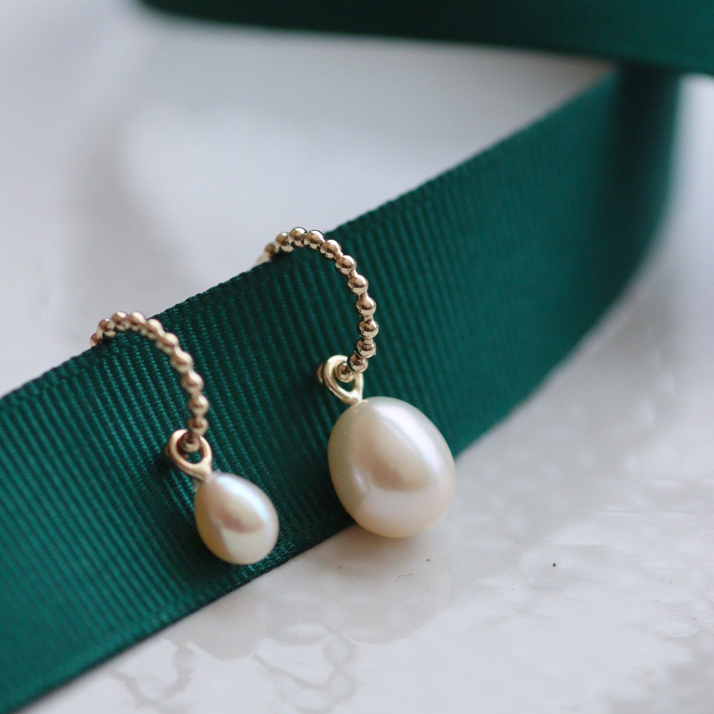 a pair of gold bubble hoop earrings with a large pearl or a small ivory pearl