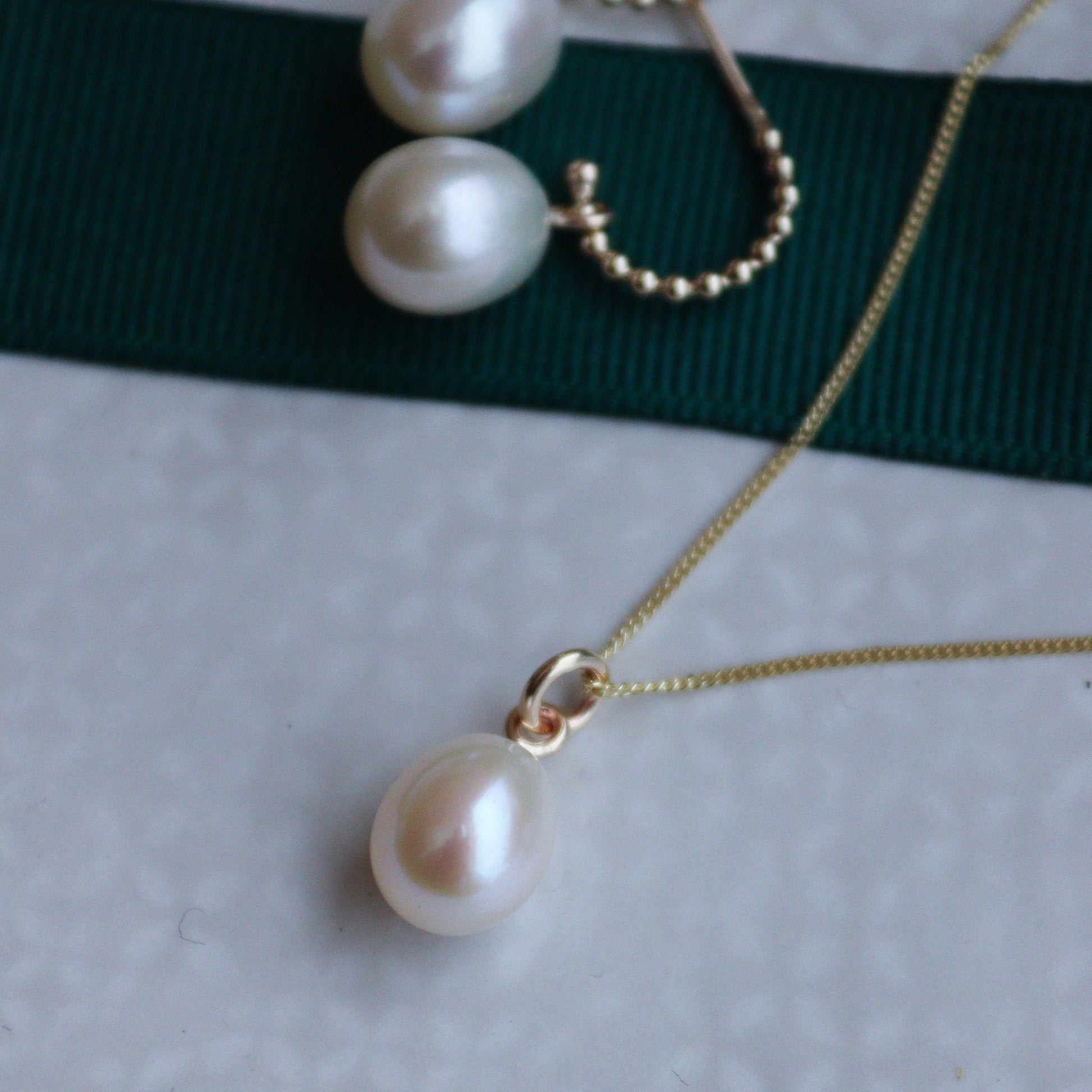 A gold pearl necklace with a diamond cut curb chain and a pearl drop, presented against a white background.