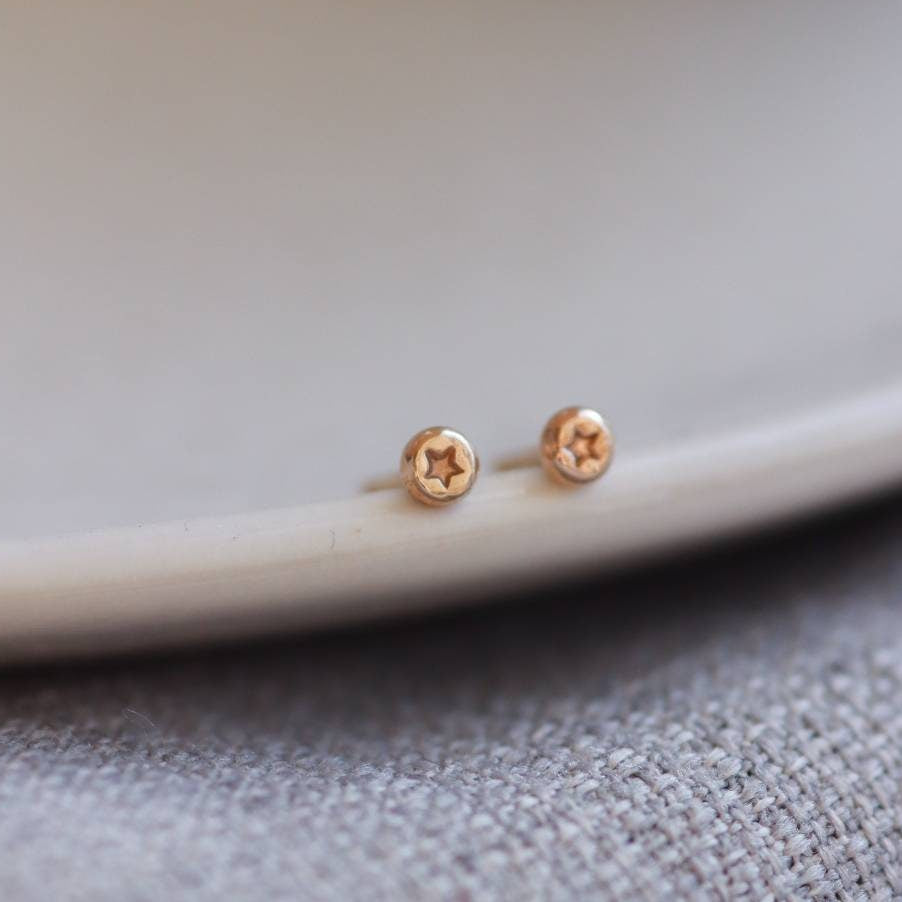 tiny gold stud earrings with a star design stamped into them on the edge of a plate.