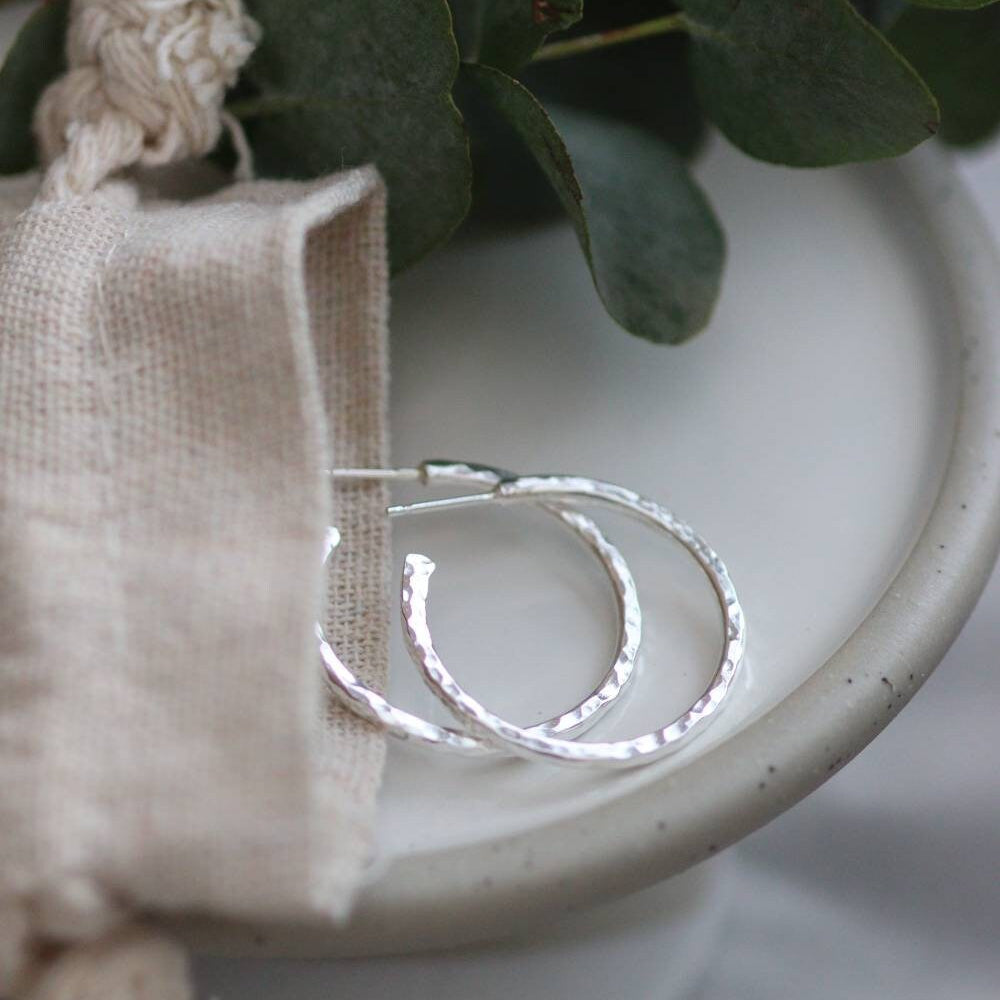 Hammered silver hoop earrings and calico pouch on a light background.
