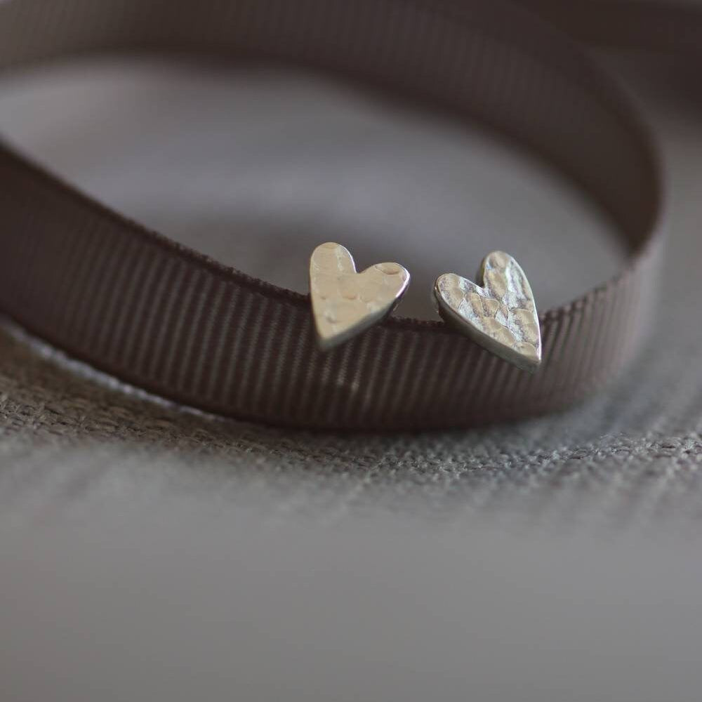chunky silver heart studs with a hammered texture, propped on a grey ribbon