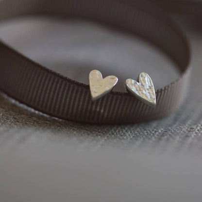 chunky silver heart studs with a hammered texture, propped on a grey ribbon