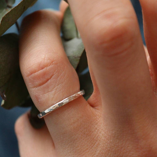 Bright silver hammered stacking ring being worn against a blue background.