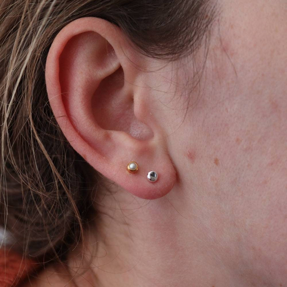 Small silver dot earrings with a heart design, being worn.