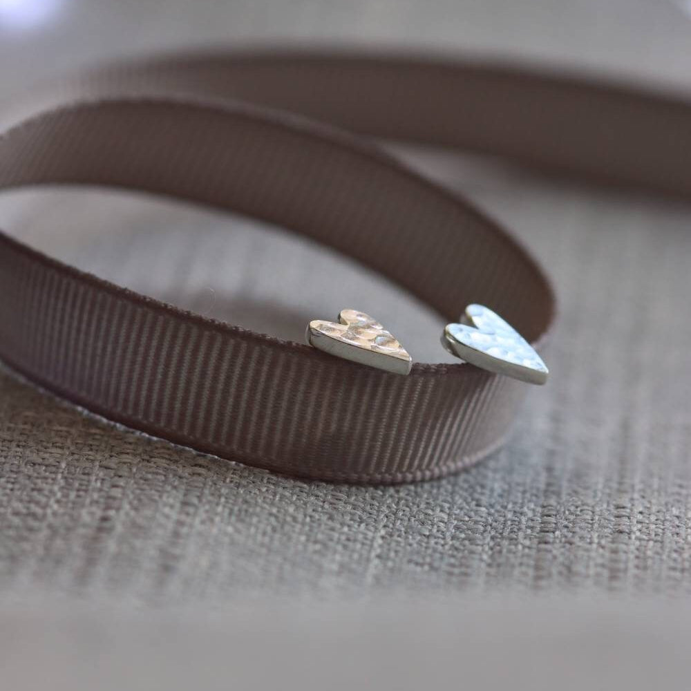 side view of hammer textured silver heart studs propped on a ribbon.