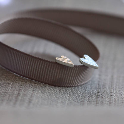 side view of hammer textured silver heart studs propped on a ribbon.