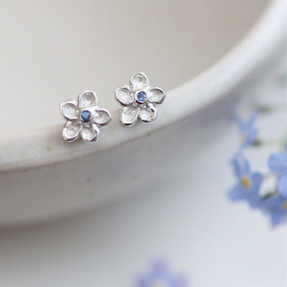 silver and sapphire flower shaped earrings on the edge of a bowl