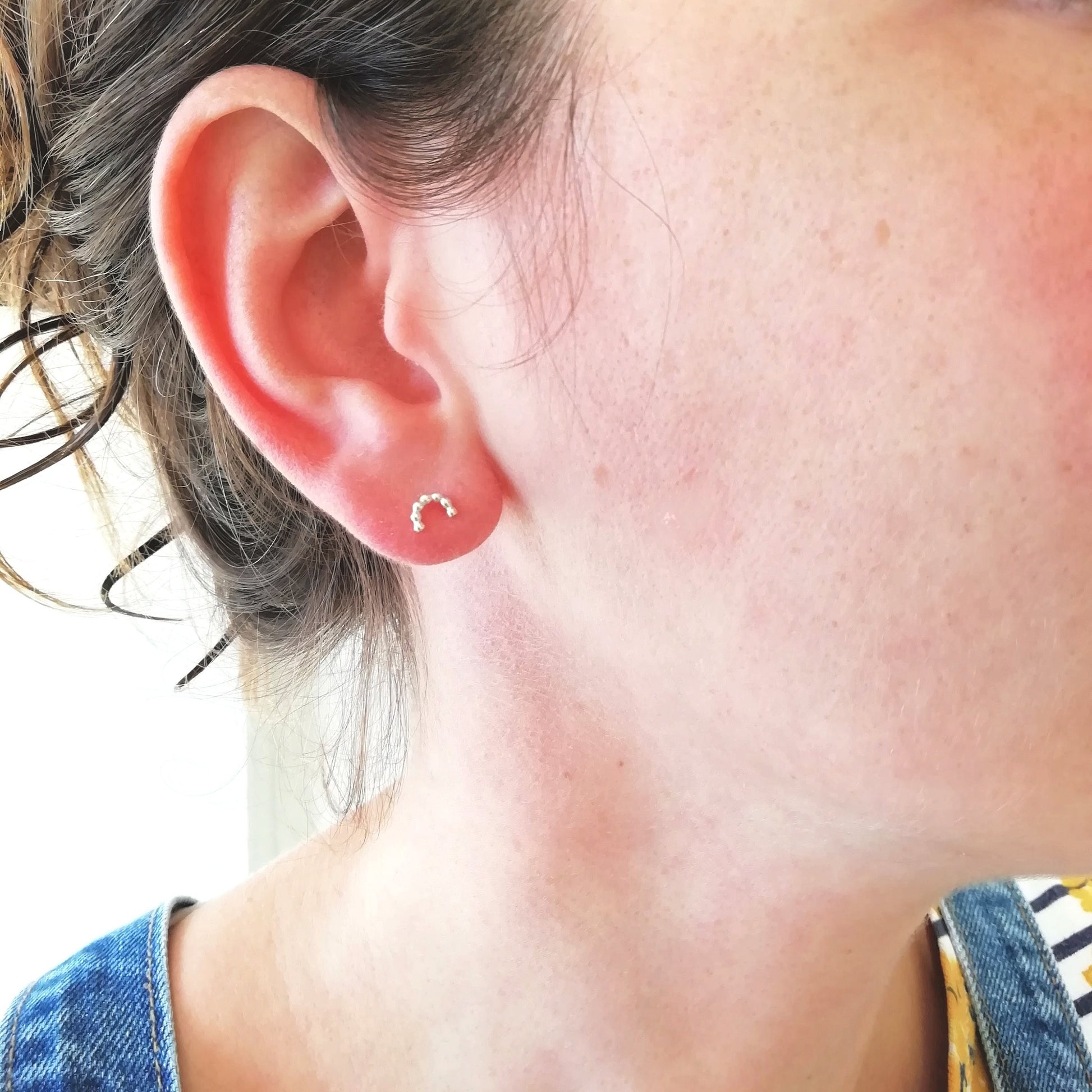 minimalist silver arc studs being worn in the earlobe.