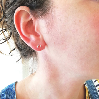 minimalist silver arc studs being worn in the earlobe.