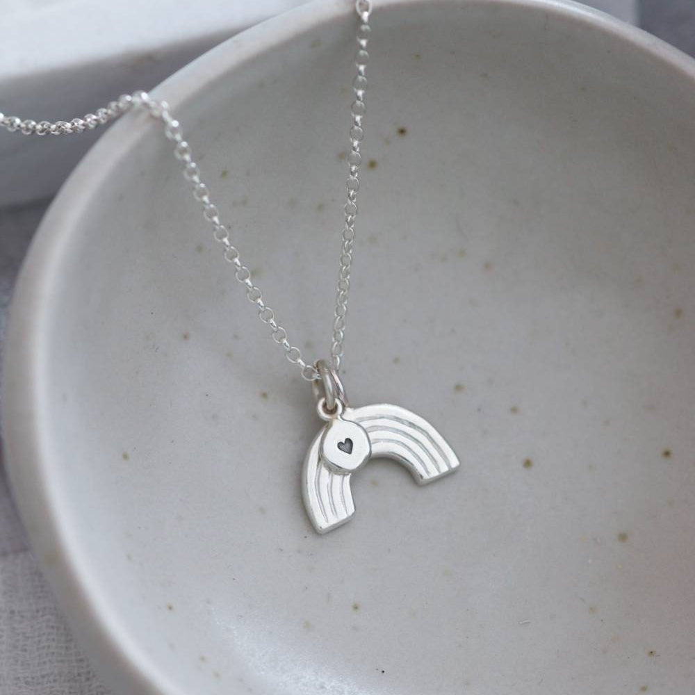 A silver necklace comprising  silver rainbow charm and a round pendant with a heart stamp.