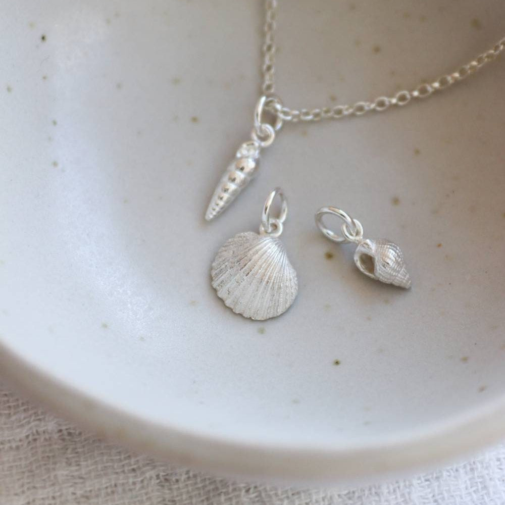 a group of 3 silver seashell charms in a dish. A spiral shell, a cornish cockle and a dorset whelk.