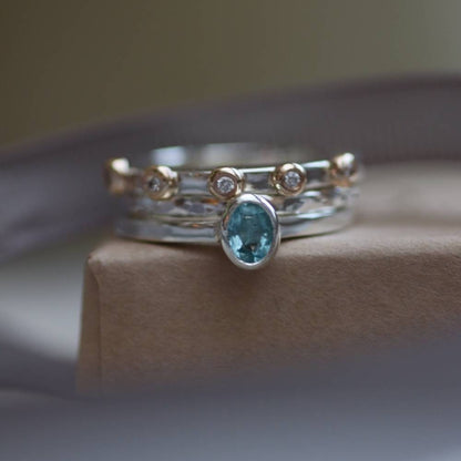 A stack of sterling silver rings one with an oval aquamarine, silver stacking ring and a silver and gold bobble ring with diamonds.