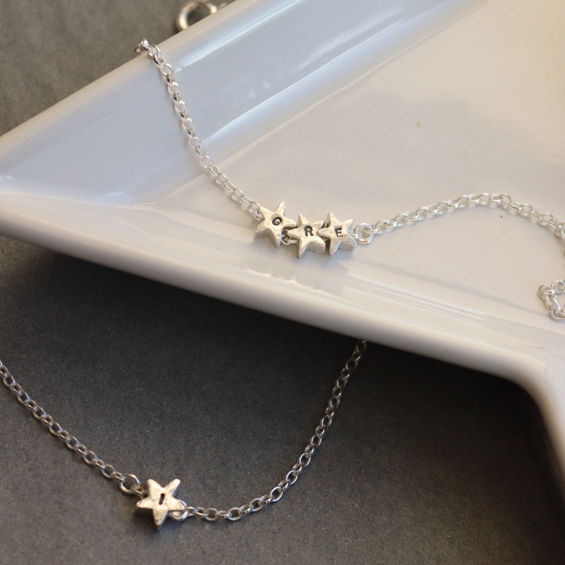 silver chain bracelets with silver star beads stamped with initials. One is a trilogy of small stars, the other in a single large star.