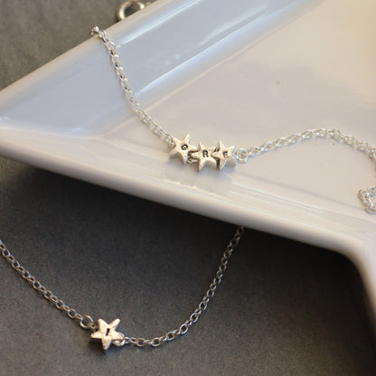 silver chain bracelets with silver star beads stamped with initials. One is a trilogy of small stars, the other in a single large star.