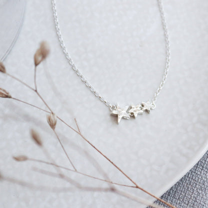 3 silver star beads graduating in size on a fine silver chain with a hammered finish.